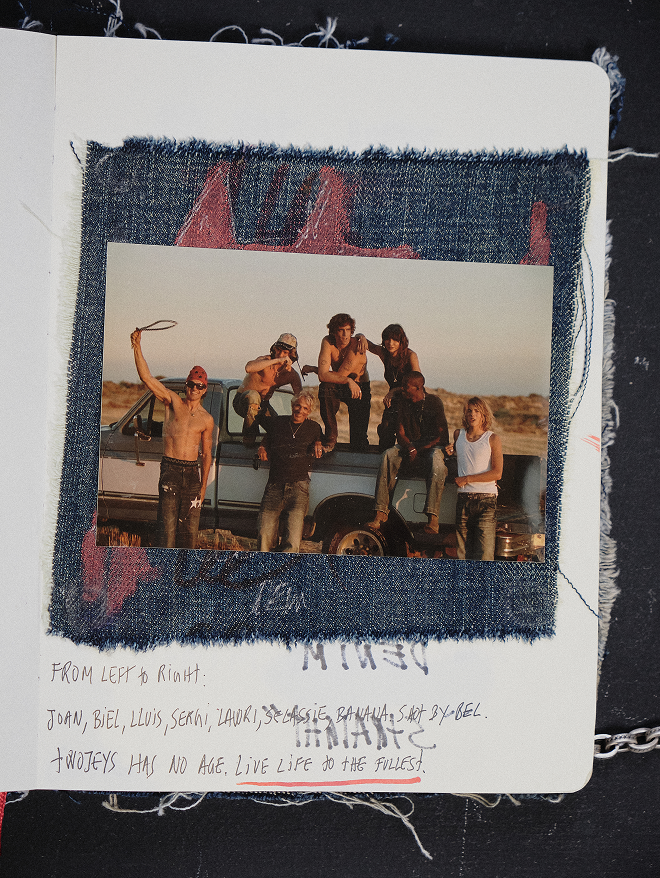 A square fabric collage or scrapbook page featuring a central photograph of a group of men standing on and around a pickup truck, bordered by dark blue denim-like material with pink stitched details. Handwritten text appears below the photo on a white paper background.