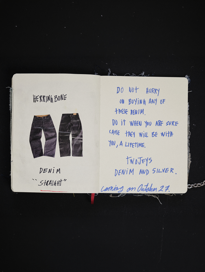 An open notebook or journal on a black background, showing a handwritten note about jeans on the left page with two small denim illustrations, and more handwritten text on the right page mentioning 'Twojets' and 'Denim and Silver.'.